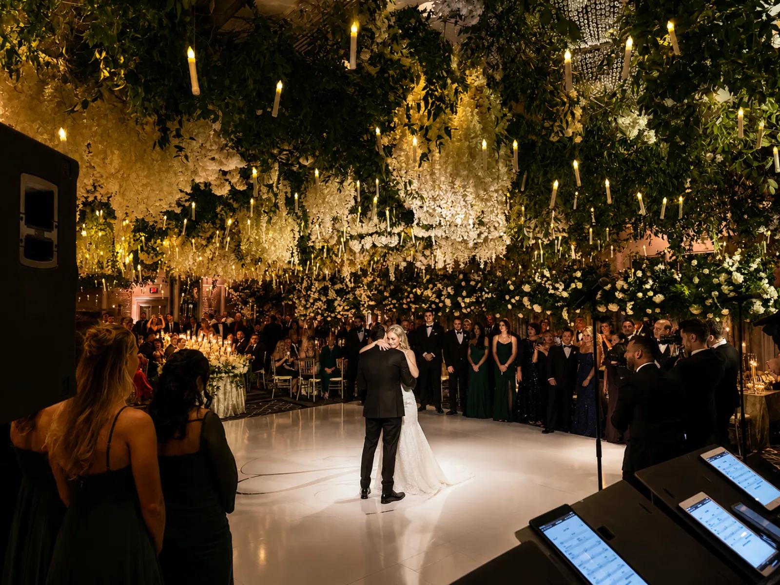 A couple's first dance on a lit floor under a floral and candlelit ceiling